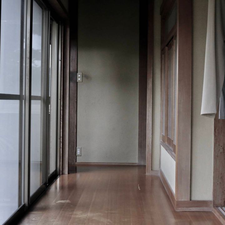 薄暗い古い廊下。外の景色と部屋の内装が見えている。