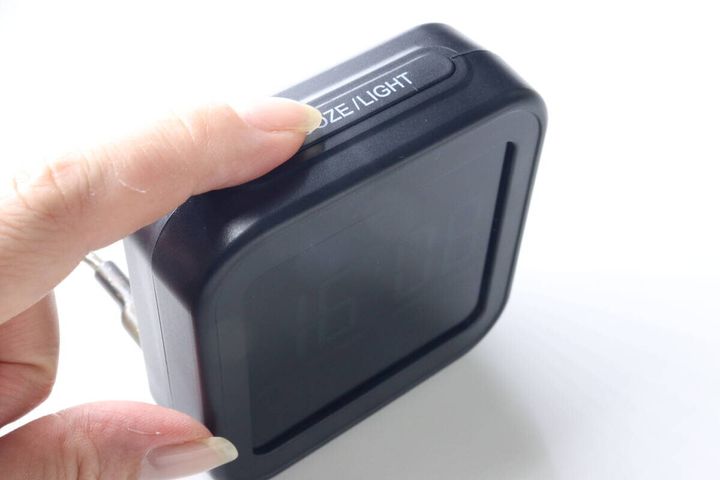 女性の指がデジタル時計上部のSNOOZE／LIGHTボタンを押している