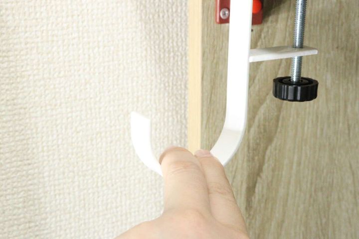 手が白いテーブルフックを木目調のテーブルの端に挟み込んでいる途中