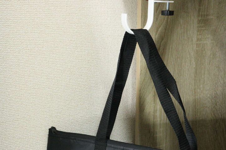 木目調のテーブルに固定された白いフックに黒いトートバッグが掛けられている
