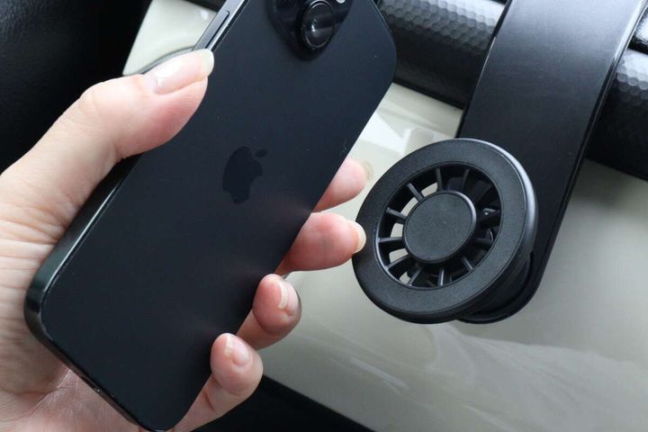 女性の手がスマートフォンを車載ホルダーのマグネット部分に近づけている