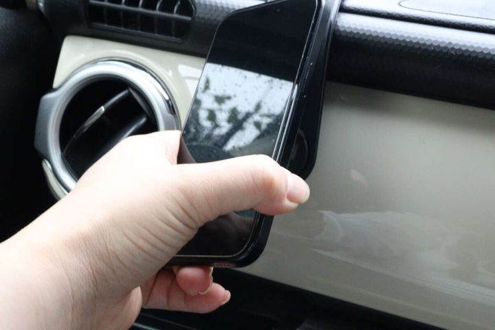女性の手がスマートフォンを車載ホルダーのマグネット部分に固定している