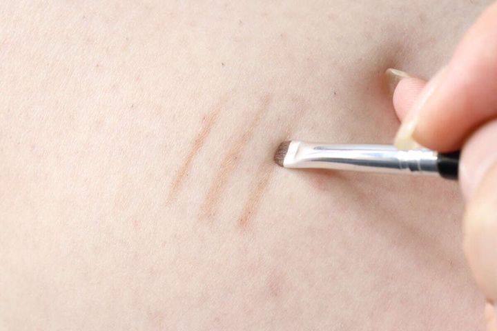 腕にアイライナーブラシで薄い茶色のラインを引く様子