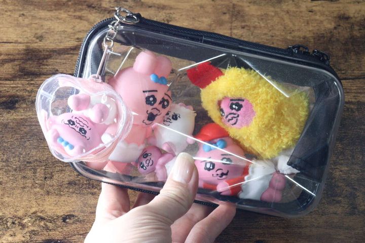 女性の手が透明なダイヤモンド形収納バッグを持ち、中にキャラクターのぬいぐるみが複数入っている