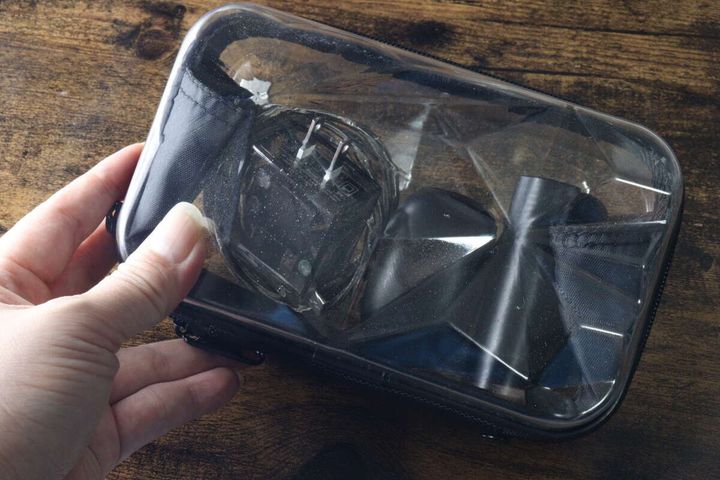 女性の手が透明なダイヤモンド形収納バッグを持ち、中にモバイルバッテリーとワイヤレスイヤホンが入っている