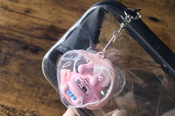透明なダイヤモンド形収納バッグのDカンに、ハート型のケースに入ったキャラクターマスコットが付けられている