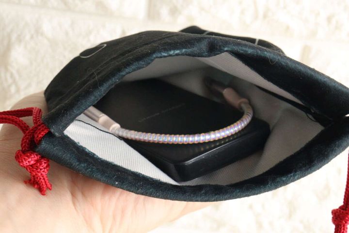 女性の手が持った黒い巾着袋の中に、モバイルバッテリーと充電ケーブルが収納されている。