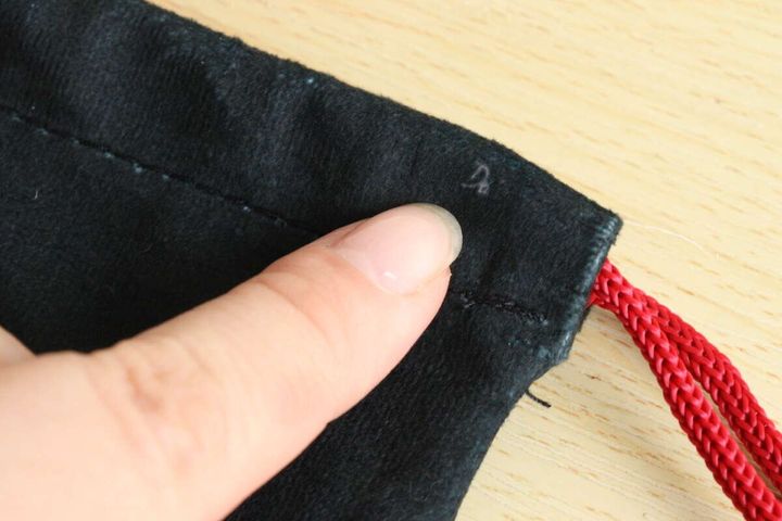 女性の指が黒い巾着袋の起毛素材の表面を指し、小さなホコリが付着している様子を示している。