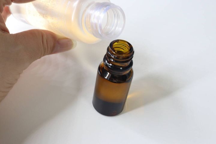 透明なボトルから茶色のスプレー容器へ液体を注ぎ入れている。