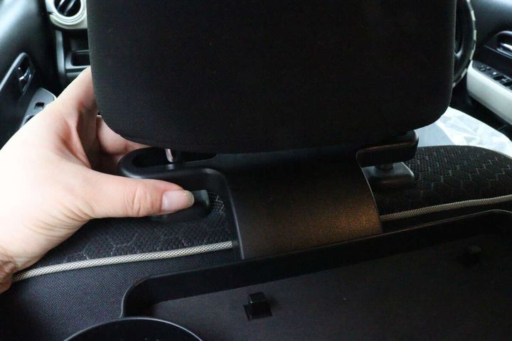 女性の手が車のヘッドレストにトレイを差し込んで取り付けている