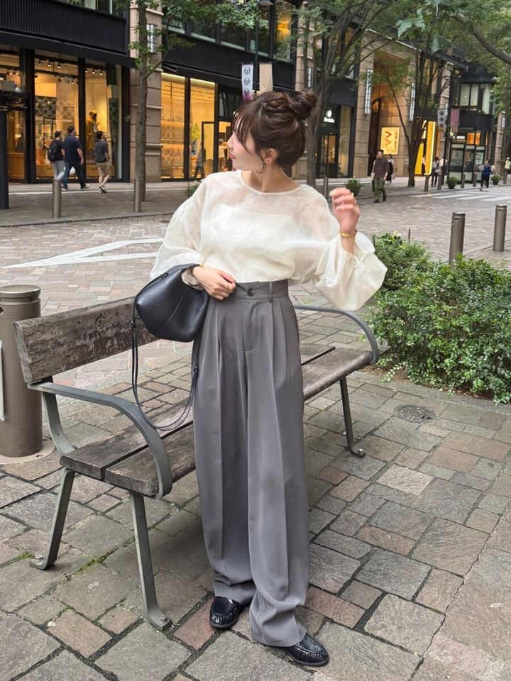 白いボリュームブラウスとグレーのワイドスラックスを着用し、街中で横を向く女性