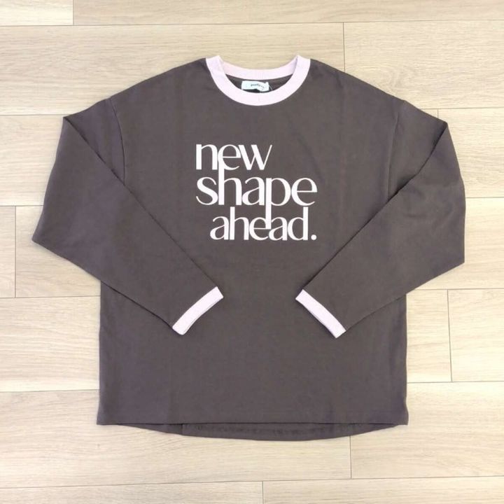 茶色の長袖Tシャツ。胸元に白文字、首元と袖口がピンクのリンガーデザイン