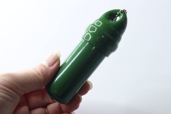 女性の手が緑色の筒状の小物入れキーホルダーを持っている