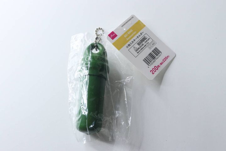 緑色の筒状の小物入れキーホルダーが透明な袋に入っている。商品タグも見える