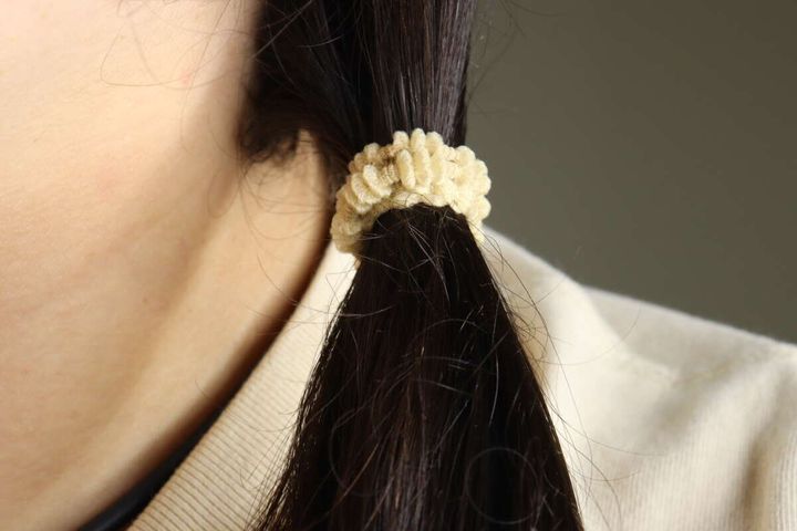女性の黒髪を淡いベージュのもこもこヘアゴムで結んだポニーテール。