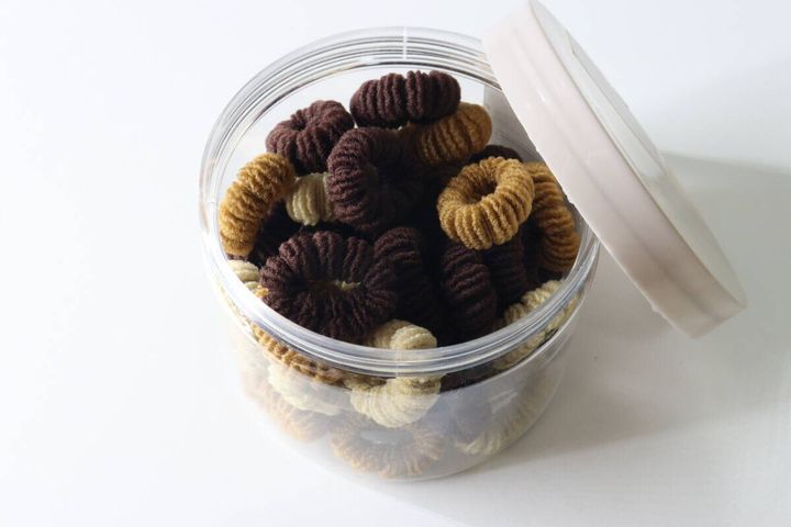 蓋が開いた透明ケースに、ブラウン系のモコモコヘアゴムがぎっしり入っている。