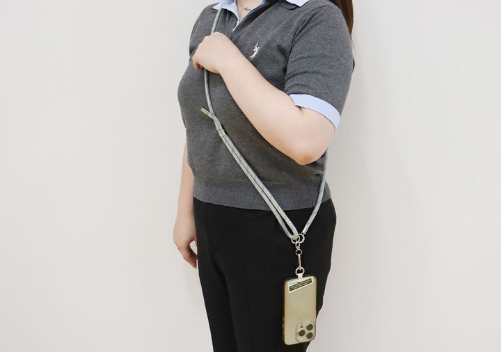 グレーのポロシャツを着た女性がスマホストラップを斜め掛けしている