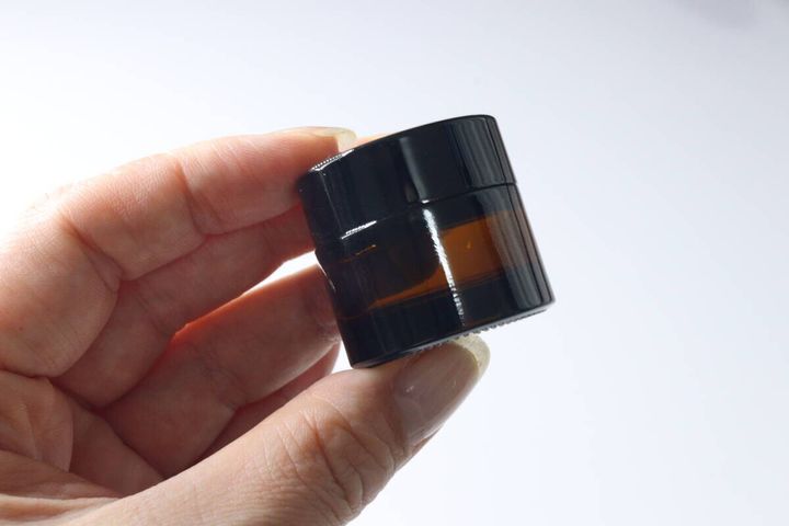 女性の手に持たれた茶色のガラス製クリームケース