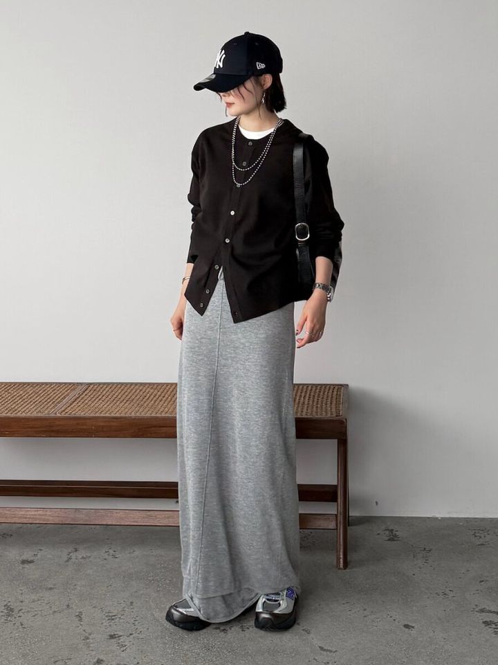黒カーディガンとグレーのロングスカートにキャップを合わせた女性