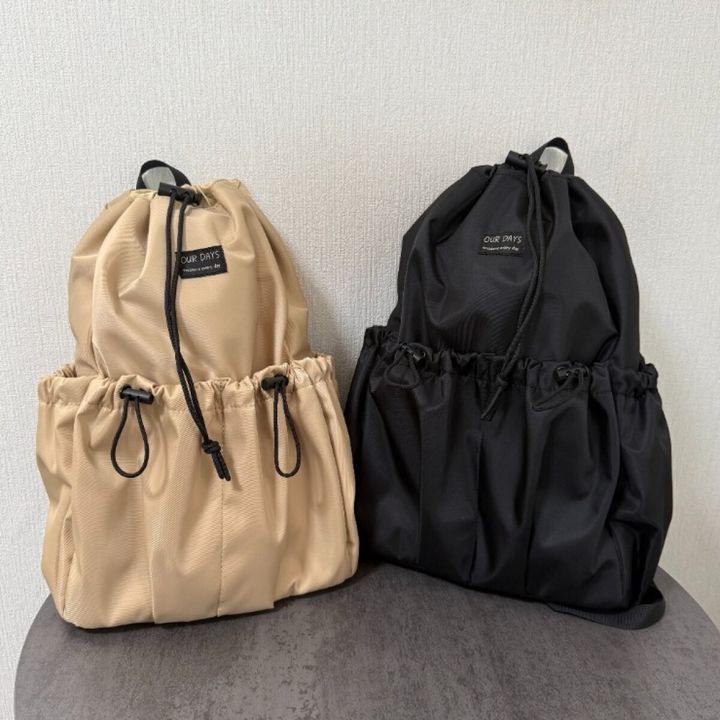 床に置かれたベージュと黒の巾着型2WAYリュック