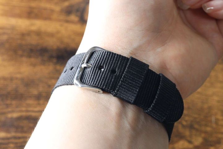 手首に装着されたミリウォッチの黒いベルトとシルバーのバックル
