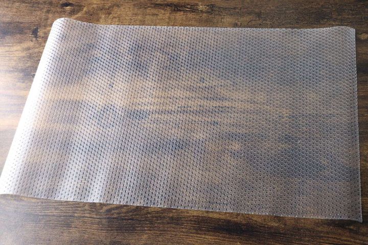 木目のテーブルに広げられた、表面に凹凸加工が施されたクリアな冷蔵庫マット
