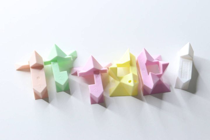 分解された6つのパステルカラーのパズルパーツが白い台の上に並べられている