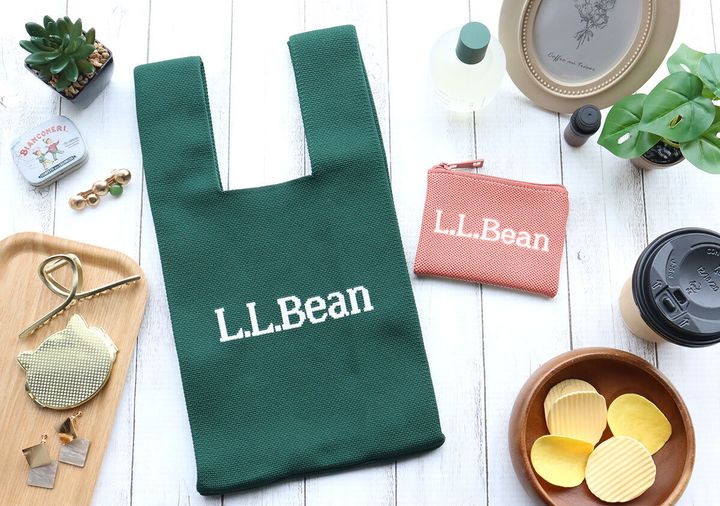 白い木目のテーブルに、緑色のL.L.Beanニットバッグとピンクのポーチ、飲み物やスナックなどが置かれている