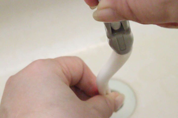 洗面台の排水口にパイプクリーナーの持ち手部分を差し込んでいる手元