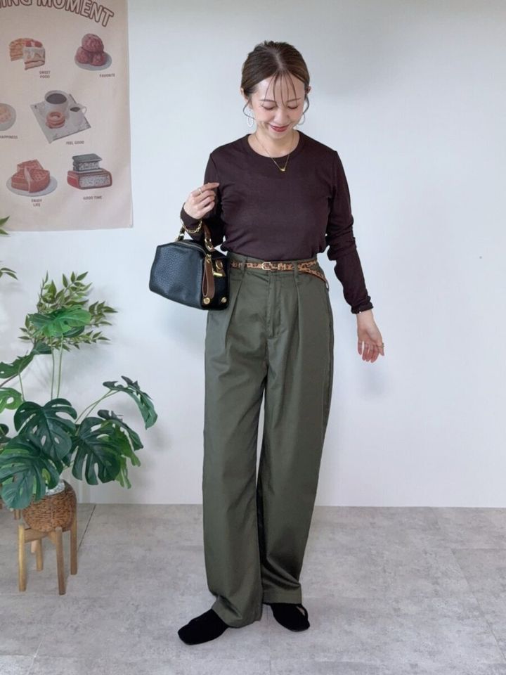 ダークブラウンシアートップスとカーキワイドパンツの女性が、黒バッグを持ち笑顔