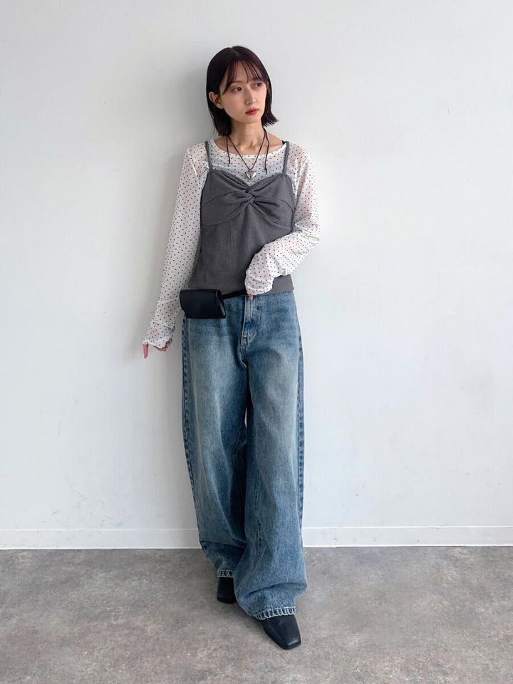 ドット柄シアートップスとビスチェ、ワイドデニムの女性が壁にもたれる