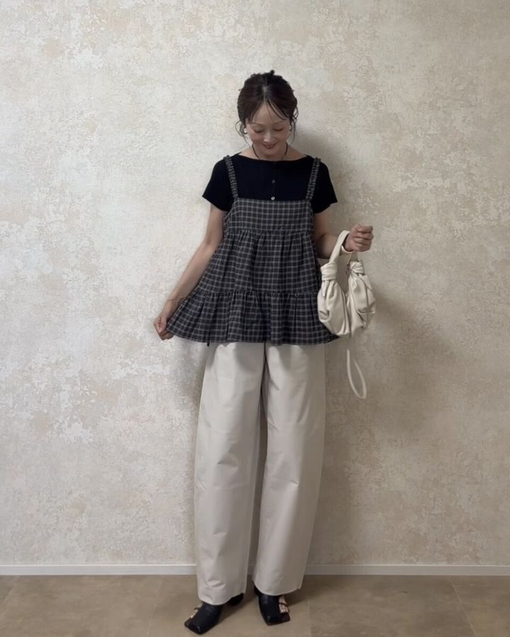 黒Tシャツと白パンツにチェックキャミを重ね着し、笑顔でポーズをとる女性の全身