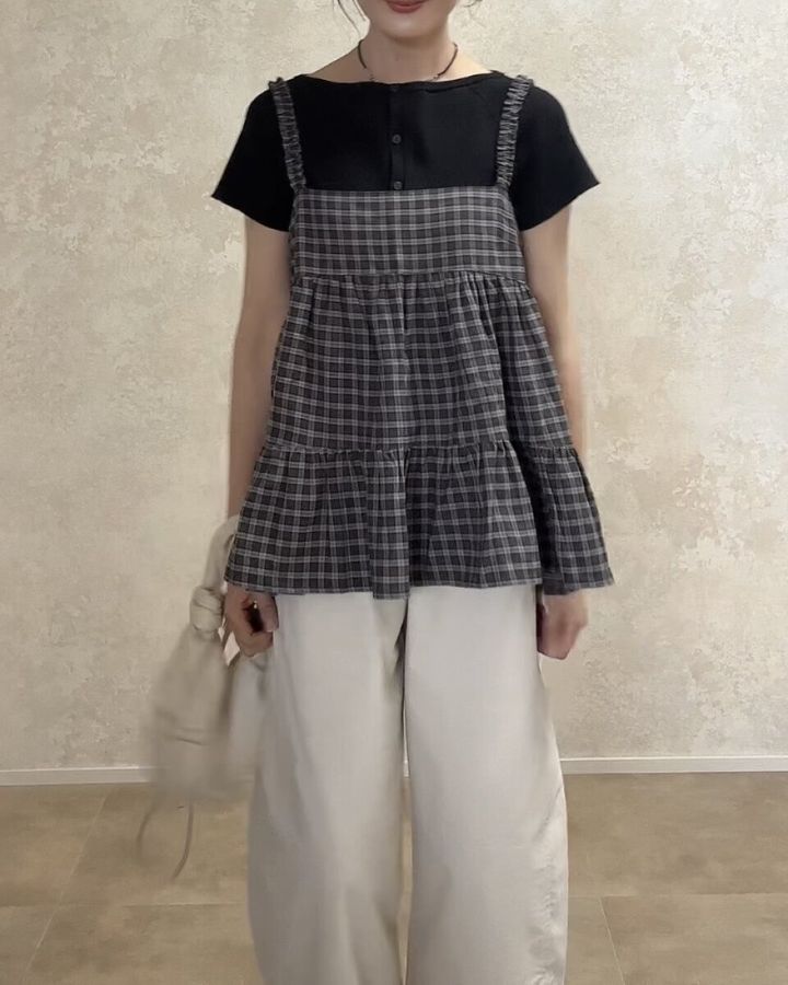 黒Tシャツと白パンツにチェックキャミを重ね着した女性が正面を向いて立っている