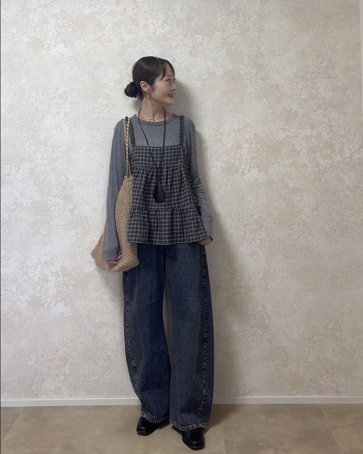グレーのロンTとデニムにチェックキャミを重ね着した女性が横を向いて立っている