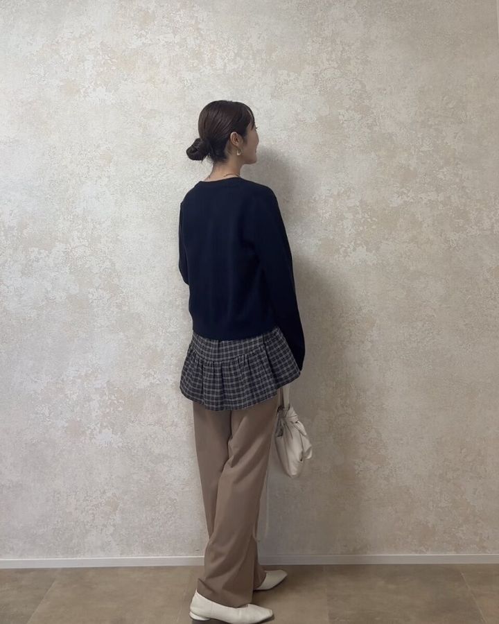 黒カーディガンとベージュパンツにチェックキャミを重ね着した女性の後ろ姿