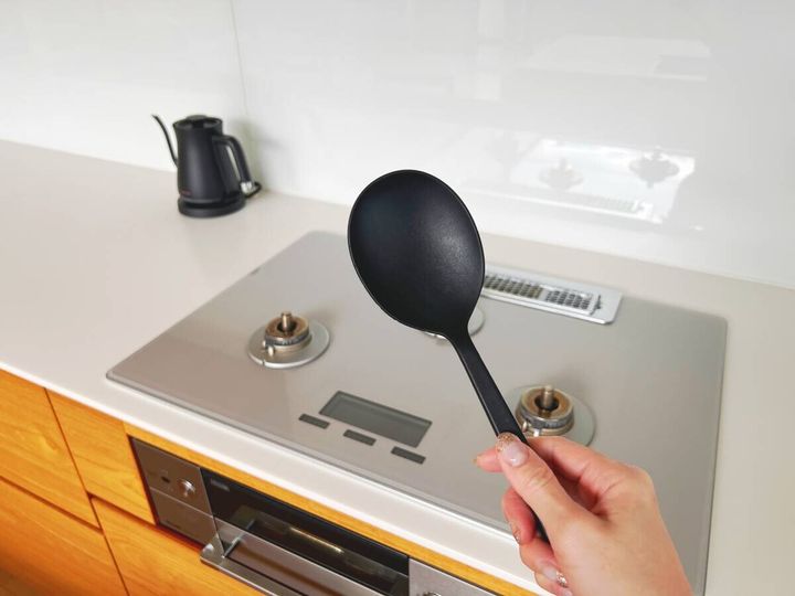 女性が黒いお玉を持っている手元とIHクッキングヒーター