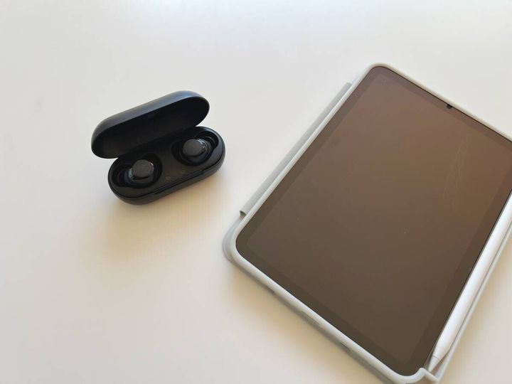 白いテーブルに置かれた黒いワイヤレスイヤホンとタブレット