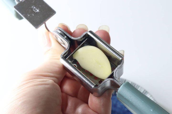 女性の手がガーリックつぶしの受け皿部分に皮をむいたにんにくを一かけ入れている