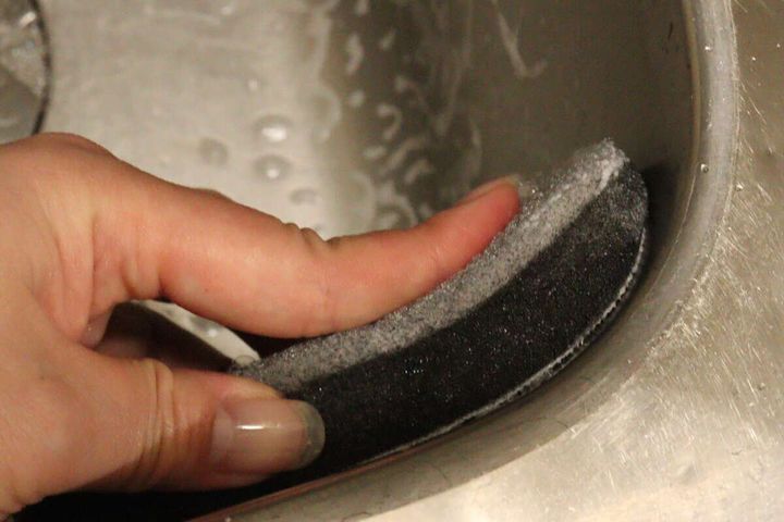 女性の手がダイソーのスポンジの黒い面でシンクのカーブ部分を掃除している