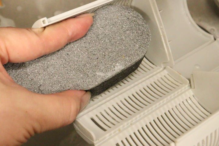 女性の手がダイソーのスポンジのグレー面でキッチンのゴミ受けを掃除している