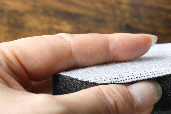 女性の指で押さえられた、ダイソーのシンク・排水口スポンジの白いブラシ面