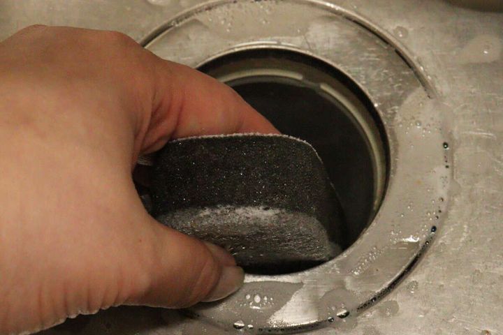 女性の手がダイソーのスポンジの黒い面でキッチンの排水口内部を掃除している