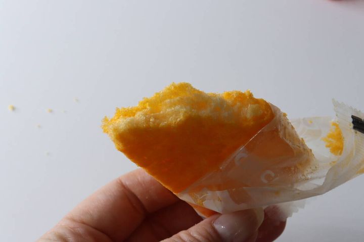 一口かじられたチーズ味ライスクラッカーを指で持っている