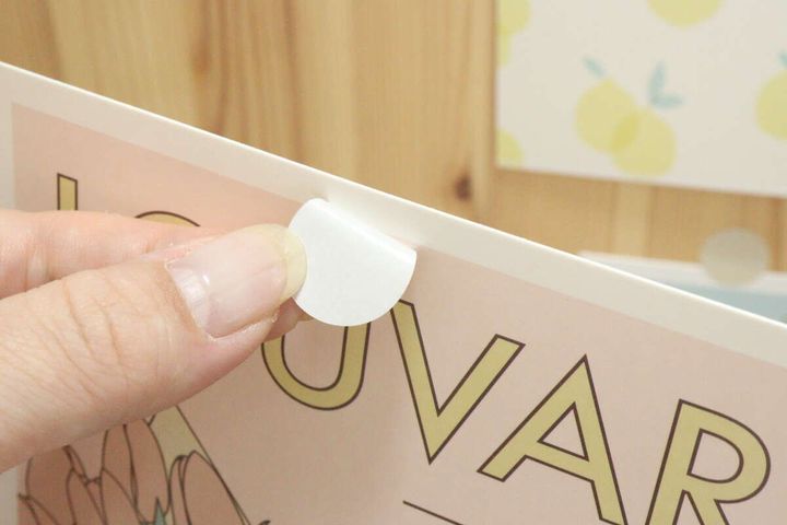 壁に貼ったカードのシールを剥がしている指先