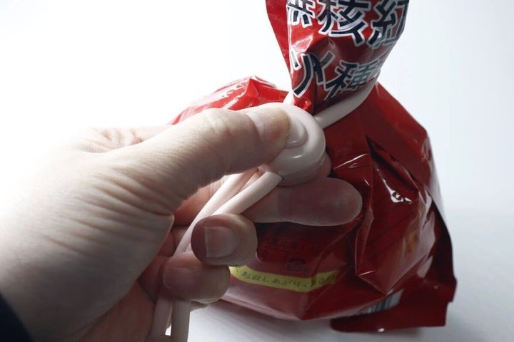 調節できる輪ゴムクリップで赤い袋の口をしっかり留めている手元