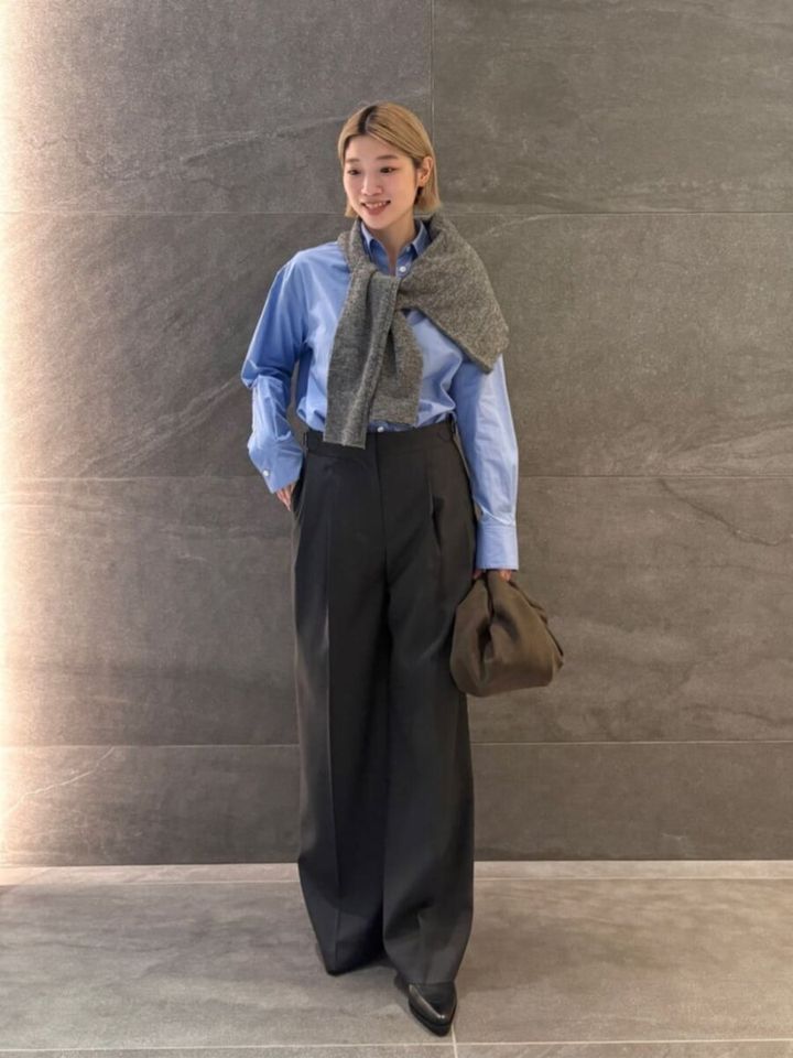ブルーシャツにグレーカーデを肩掛けしたきれいめスタイルの女性