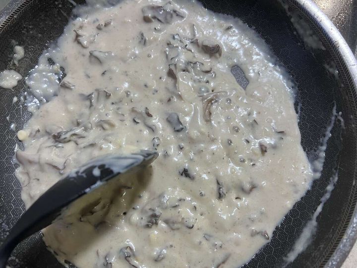 フライパンで舞茸と混ぜたクリームソースをゴムベラで混ぜながら煮詰めている様子