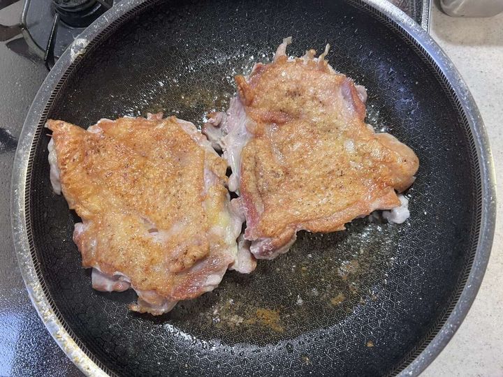 フライパンで鶏もも肉2枚の皮目をきつね色に焼いている様子