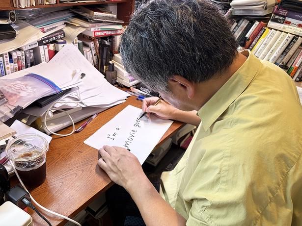 仕事場のデスクでメッセージを書く是枝監督