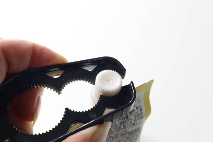 マルチキャップオープナーでパウチ容器の白いキャップを開ける手元